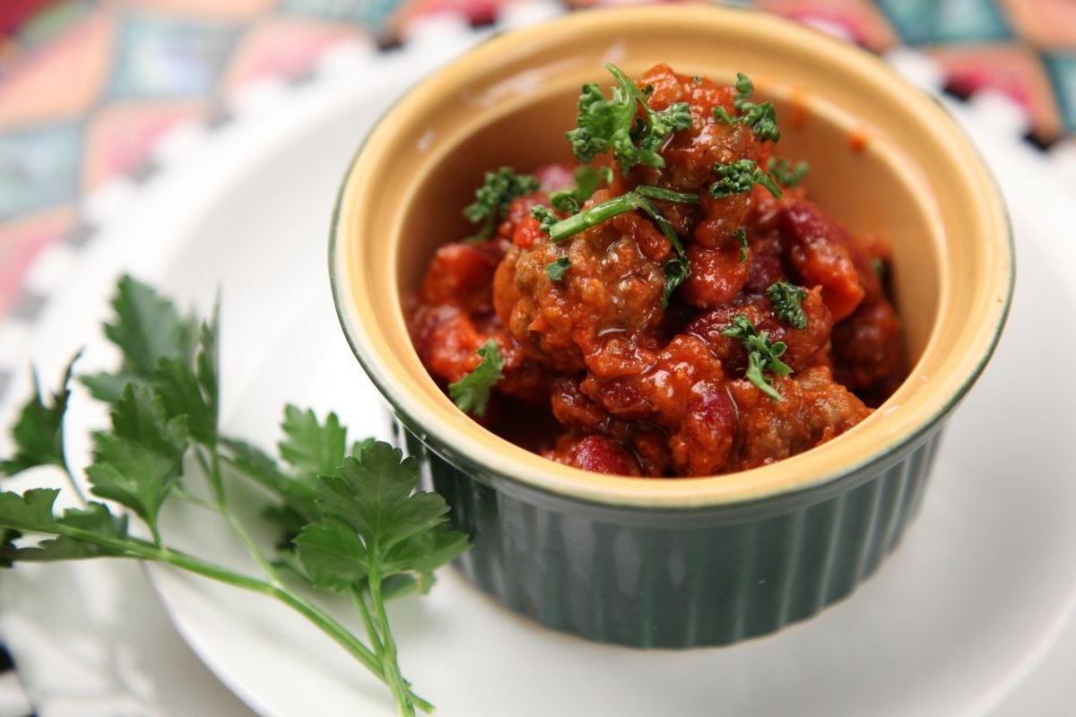 Bowl of beef and bean chili garnished with fresh herbs