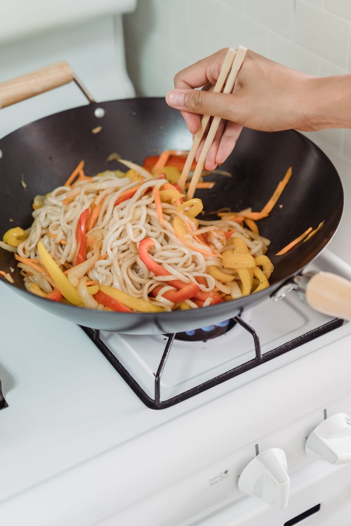 Noodles and sliced vegetables being tossed in a wok with chopsticks